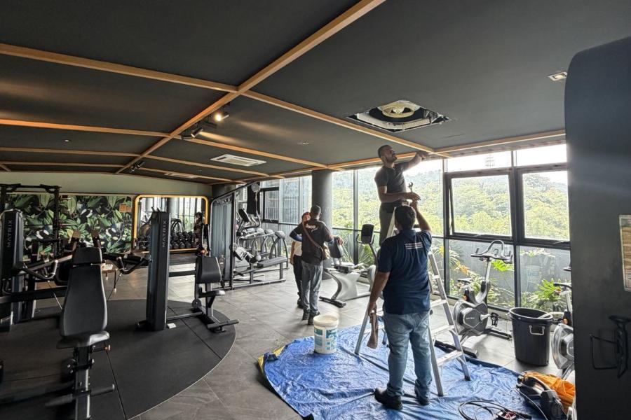 Two technicians servicing a gym cassette with the floor tarped