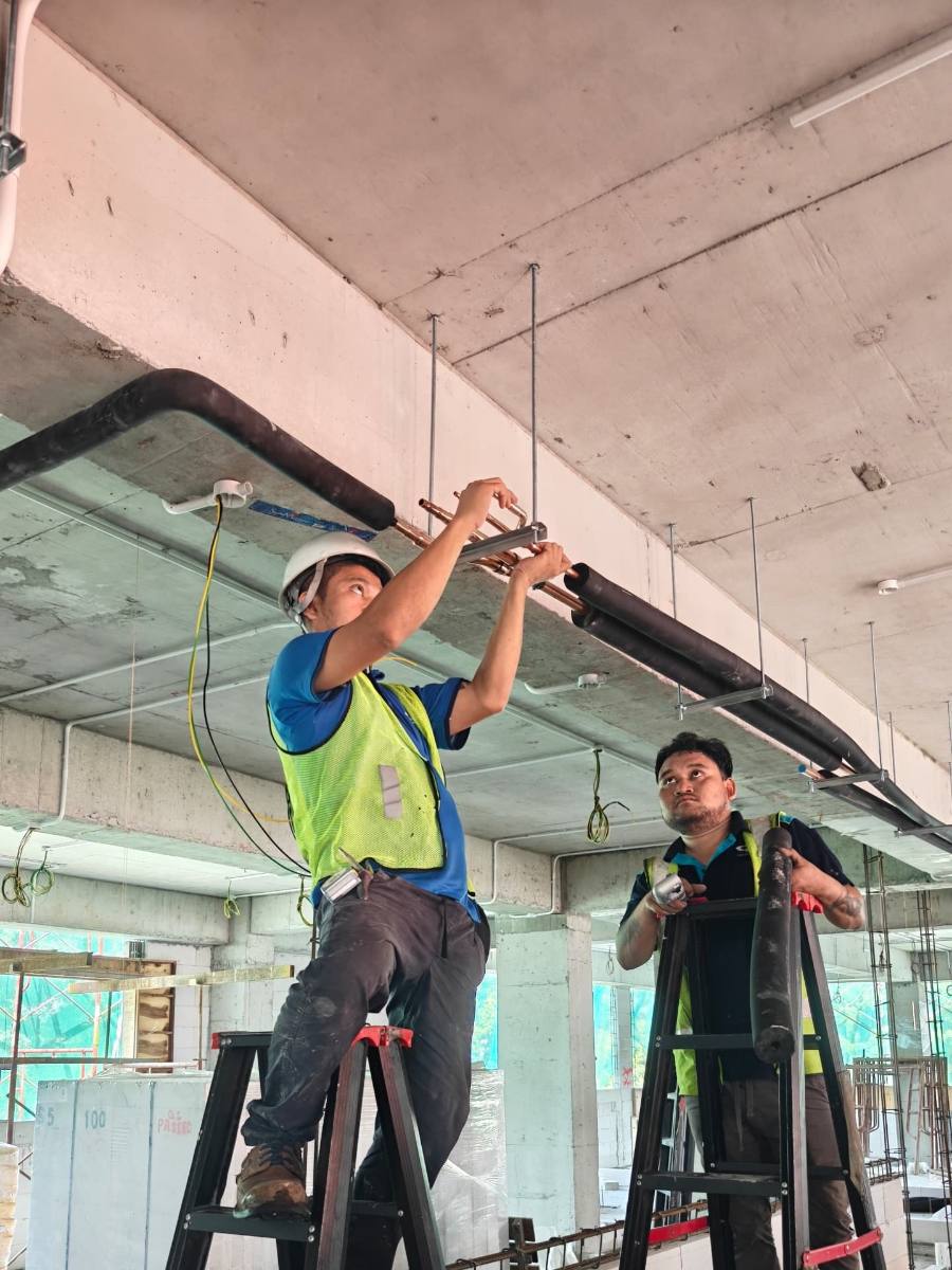Technicians installing insulated refnet branch piping at ceiling level